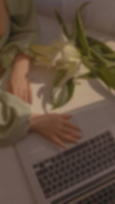 a close up of a person typing on a laptop with flowers in front of them