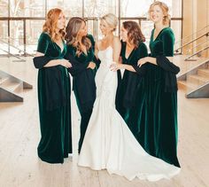 a group of women standing next to each other in front of a window wearing green velvet dresses