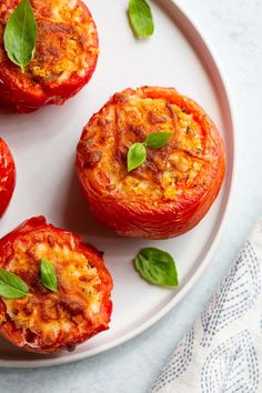 four stuffed tomatoes on a plate with basil leaves