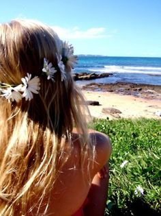 the back of a woman's head with flowers in her hair and an ocean view