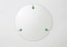 a round mirror on the wall with three green balls hanging from it's sides