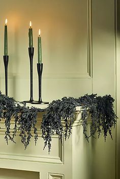 three candles are lit in front of a mantle decorated with greenery and ivy garland