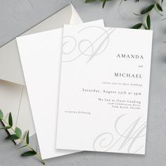 two white wedding cards with silver monogrammed lettering on them next to an envelope