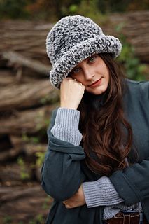 a woman wearing a hat and sweater posing for the camera with her hands on her head