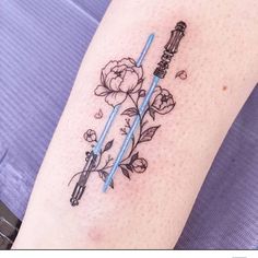 a star wars tattoo with two lightsabes and flowers on the arm, one is blue