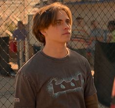 a young man standing in front of a chain link fence