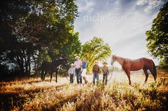 three men standing next to two horses in a field