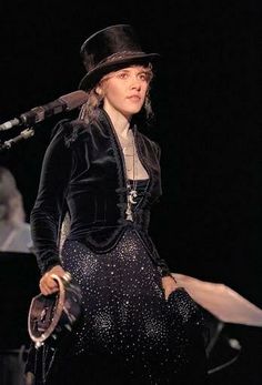 a woman in a black dress and hat on stage