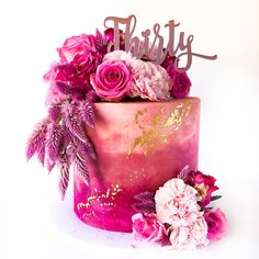 a pink and gold birthday cake with flowers on the top is adorned with a name sign