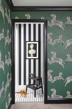 a black and white striped room with zebras on the wall, an animal print rug and a stool