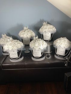 six white roses in silver vases on top of a bench with black and white trim