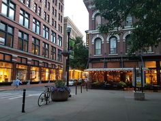 people are walking down the street in front of shops and restaurants at dusk, with their bikes parked on the sidewalk