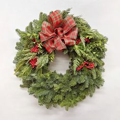 a christmas wreath with red berries and green evergreen leaves on it, hanging from the wall