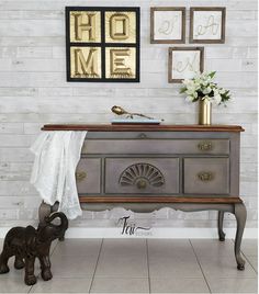 an old dresser is painted gray with gold accents and flowers on top, along with pictures above it