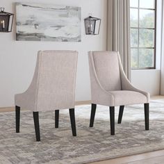 two beige chairs sitting on top of a rug in front of a wall mounted painting