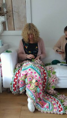 two women sitting on a white couch with crocheted afghans in front of them