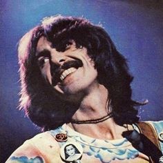 a man with long hair and mustaches on his face playing an electric guitar in front of a blue background