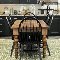 a kitchen with black cabinets and wooden table surrounded by chairs in front of the counter