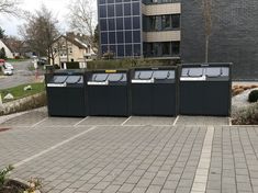 a row of black trash cans sitting on the side of a road next to a building