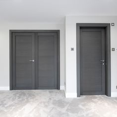 two black doors in an empty room with white walls and carpeted flooring on either side