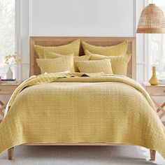 a bed with yellow comforters and pillows in a room next to a lamp on a table