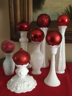 red and white vases with ornaments in them on a red table cloth next to a painting