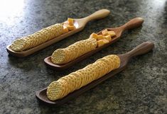 three wooden spoons with cheddar crackers on them sitting on a counter