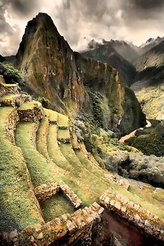 an ancient structure in the middle of a mountain range with green grass on it's sides