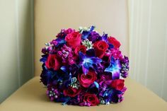 a bridal bouquet with purple and red flowers sits on a chair in front of a wall