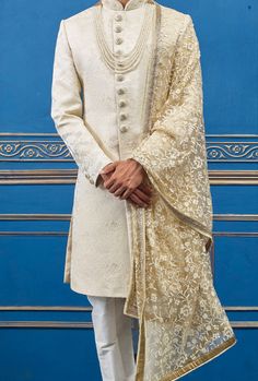 a man in a white sherwa with gold thread work on the jacket and pants