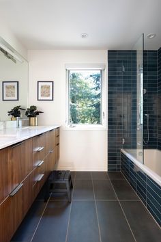 a bathroom with blue tile and wooden cabinetry next to the bathtub is shown