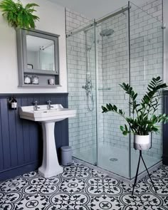 a white sink sitting under a bathroom mirror next to a walk in shower and a potted plant