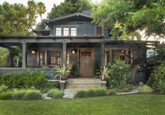 a house that is in the middle of some bushes and trees with plants around it