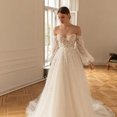 a woman in a wedding dress is standing near a window