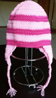 a pink and white knitted hat sitting on top of a metal stand next to a black table