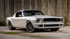 a white mustang parked in front of a wooden fence