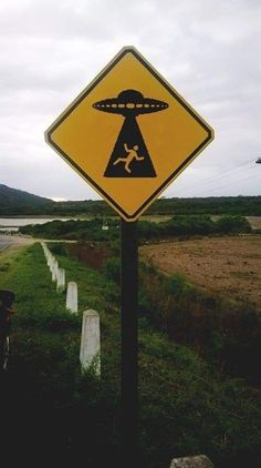 a yellow sign with an alien crossing on it's side next to a road