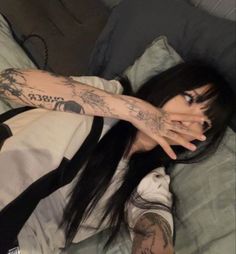 a woman laying in bed with tattoos on her arm and hand over her face, covering her eyes