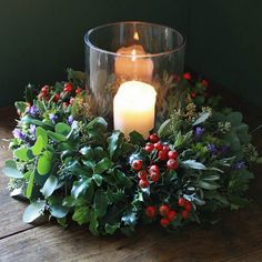 a candle sitting on top of a table surrounded by greenery and holly wreaths