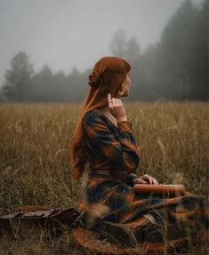 a woman with red hair sitting in a field