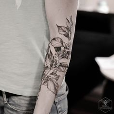 a woman's arm with flowers on it and leaves around the arm, in black and white