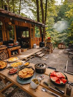 a picnic table with food on it in front of a small cabin surrounded by trees