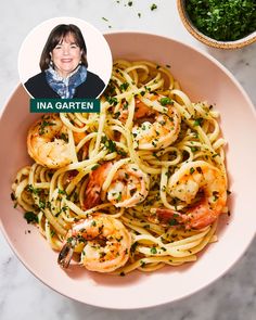 a pink bowl filled with pasta and shrimp on top of a white table next to a green salad