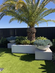 two large white planters with plants in them on artificial grass near a black fence