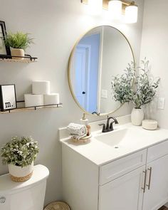 a white bathroom with a round mirror above the sink and shelves on the wall next to the toilet