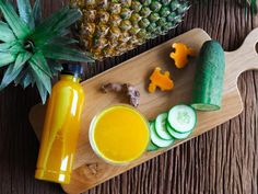 pineapple, cucumber, and orange juice on a cutting board next to sliced fruit