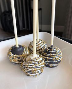 four cake pops with white and gold sprinkles on a plate next to two candles