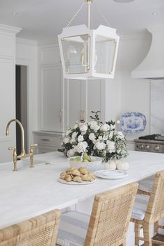 a white kitchen with flowers and plates on the counter top, along with wicker chairs