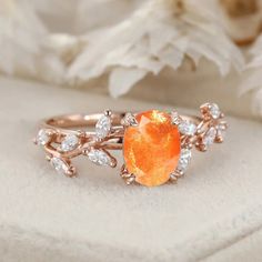 an orange stone surrounded by white diamonds sits on top of a piece of cloth next to flowers