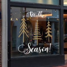 a store front window with christmas trees in the window and it's saying tis the season